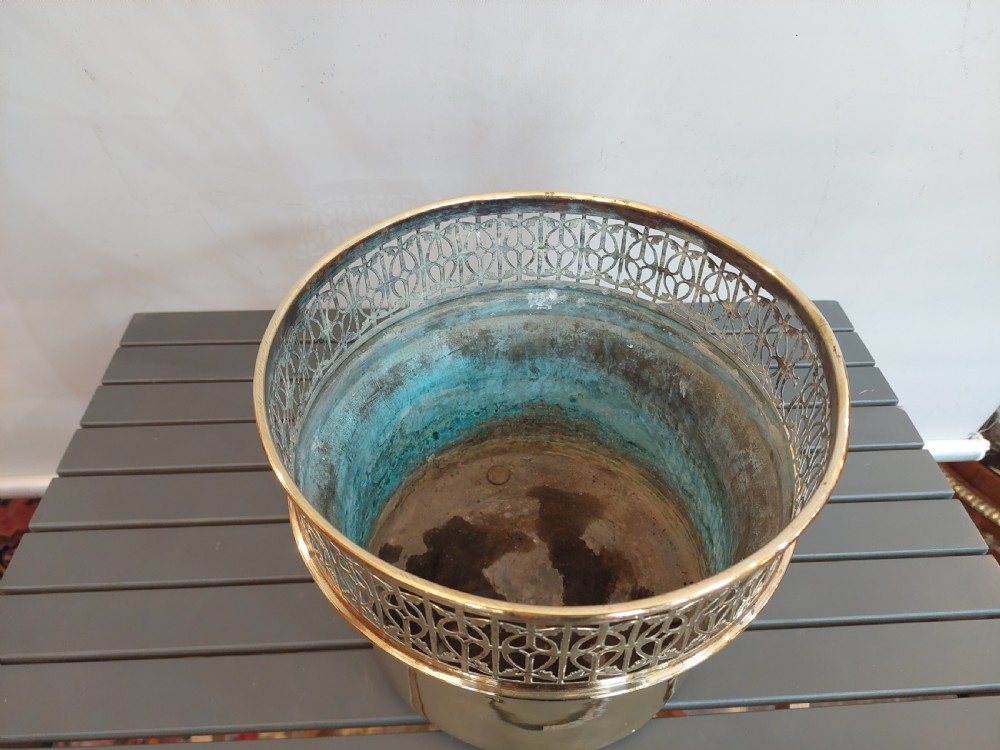 A cylindrical polished brass planter featuring a decorative pierced fretwork border near the upper rim and raised on small feet. View III