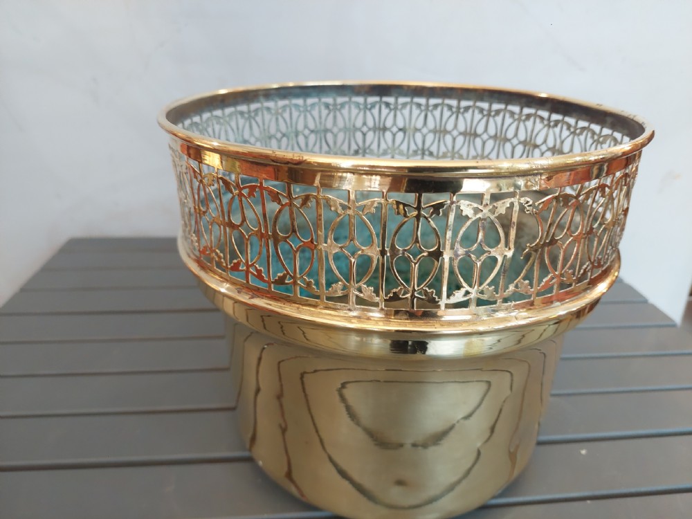 A cylindrical polished brass planter featuring a decorative pierced fretwork border near the upper rim and raised on small feet. View V