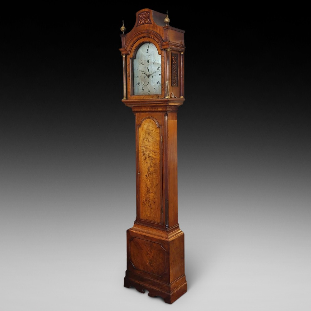 An 18th-century Georgian mahogany longcase clock featuring a pedimented hood with brass finials, an arched dial, and a flame mahogany trunk door.