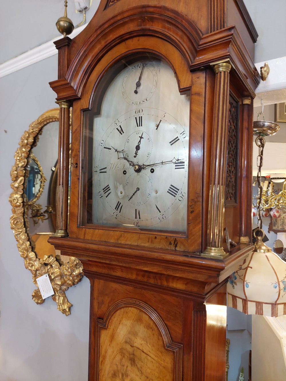 An 18th-century Georgian mahogany longcase clock featuring a pedimented hood with brass finials, an arched dial, and a flame mahogany trunk door. View V