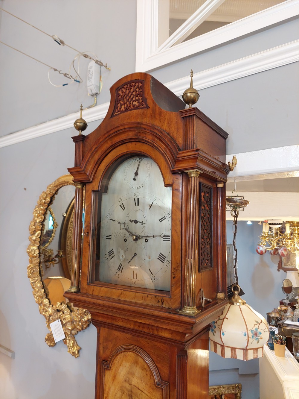 An 18th-century Georgian mahogany longcase clock featuring a pedimented hood with brass finials, an arched dial, and a flame mahogany trunk door. View VI