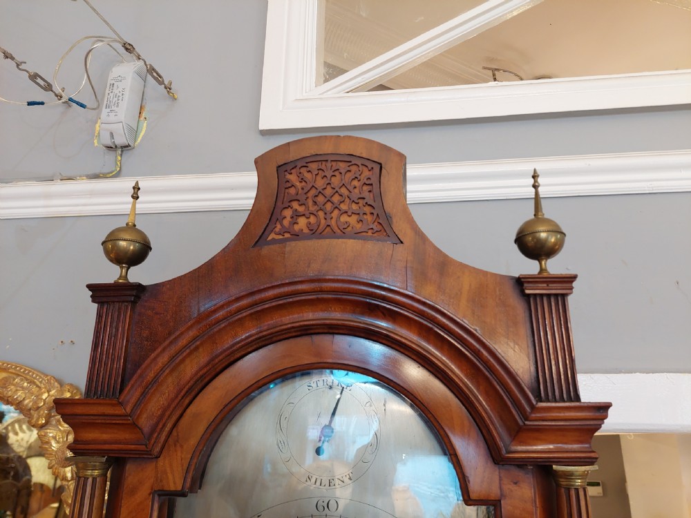 An 18th-century Georgian mahogany longcase clock featuring a pedimented hood with brass finials, an arched dial, and a flame mahogany trunk door. View VII