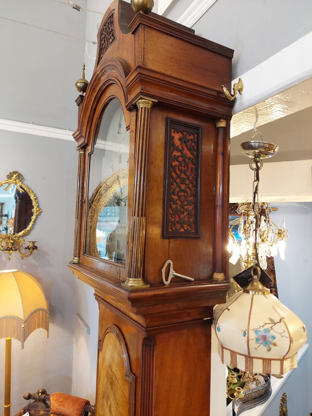 An 18th-century Georgian mahogany longcase clock featuring a pedimented hood with brass finials, an arched dial, and a flame mahogany trunk door. View IX