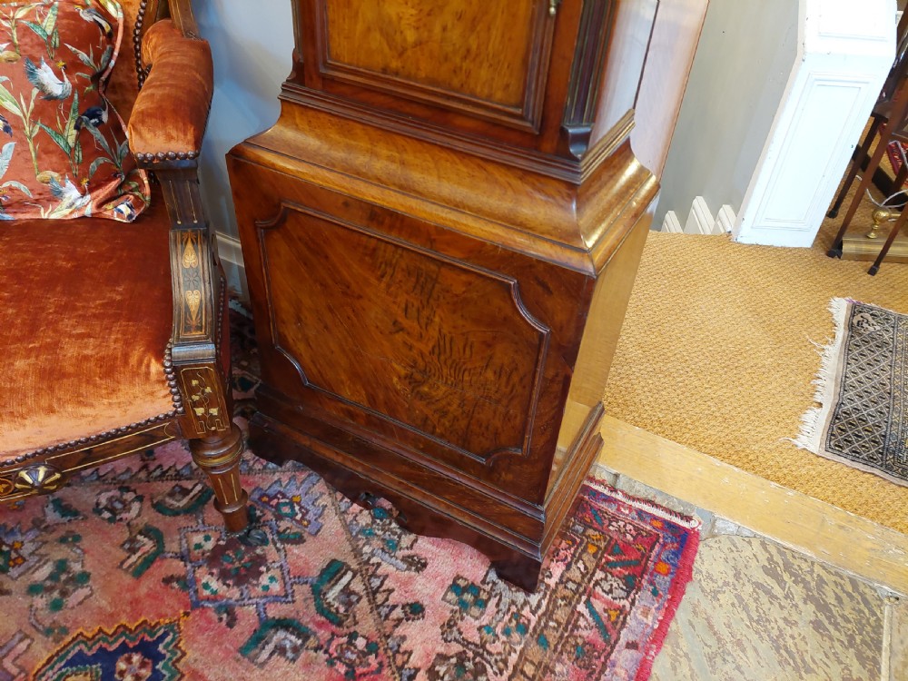 An 18th-century Georgian mahogany longcase clock featuring a pedimented hood with brass finials, an arched dial, and a flame mahogany trunk door. View X