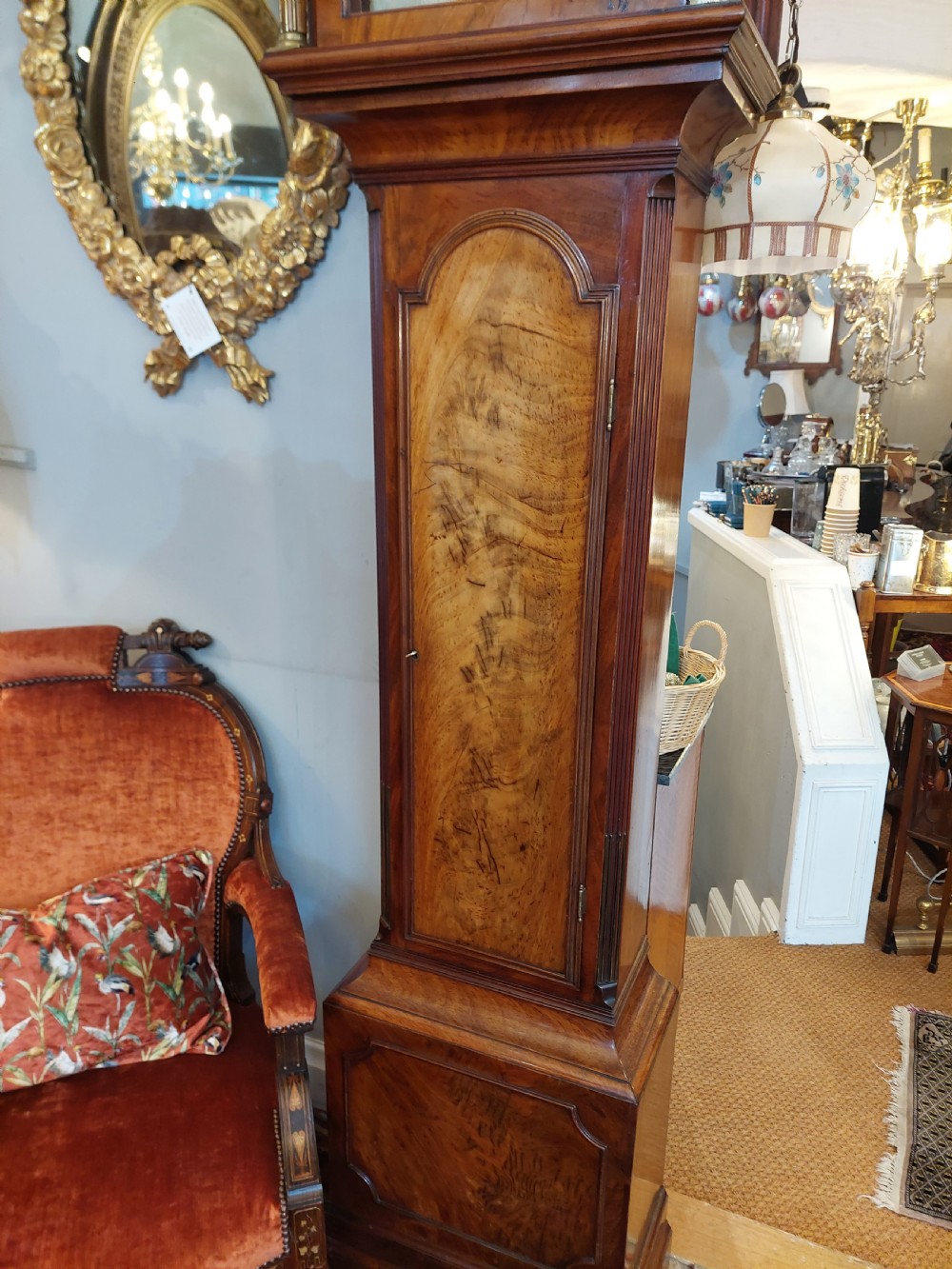 An 18th-century Georgian mahogany longcase clock featuring a pedimented hood with brass finials, an arched dial, and a flame mahogany trunk door. View XI