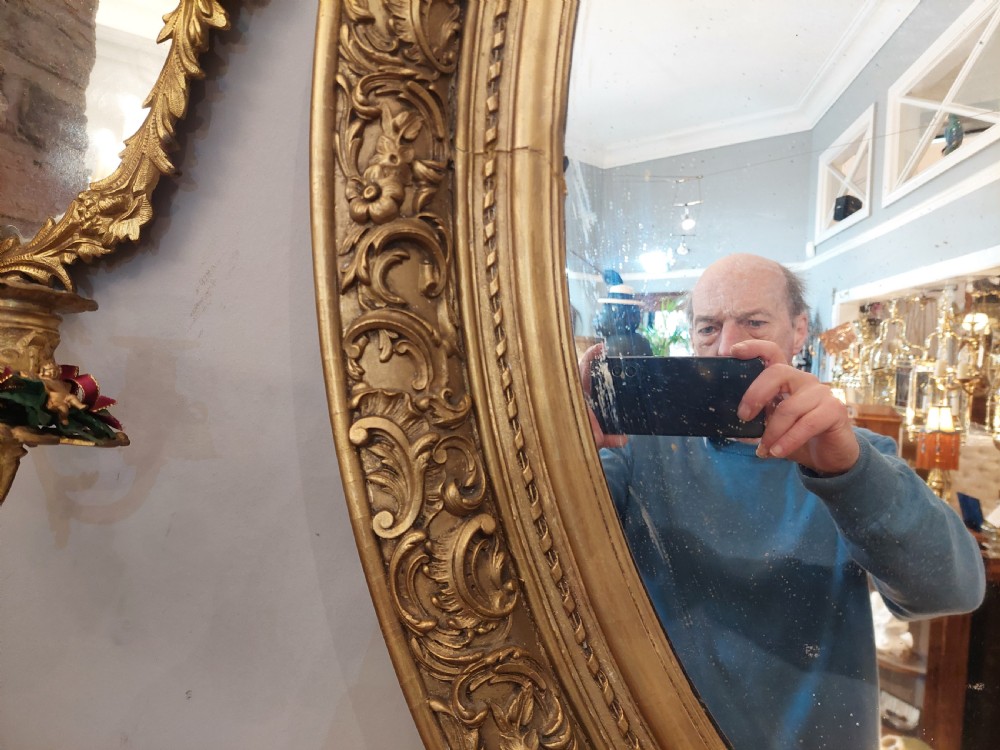 A nineteenth-century oval wall mirror featuring a heavily carved giltwood frame with floral and scrolling moulding details. View III