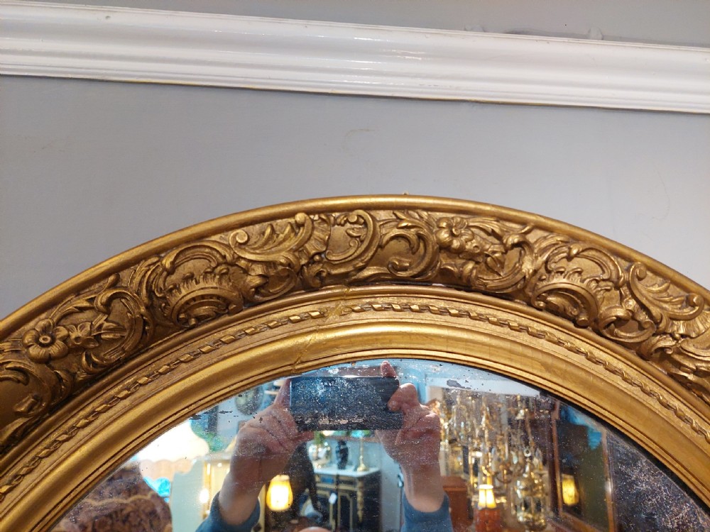 A nineteenth-century oval wall mirror featuring a heavily carved giltwood frame with floral and scrolling moulding details. View IV
