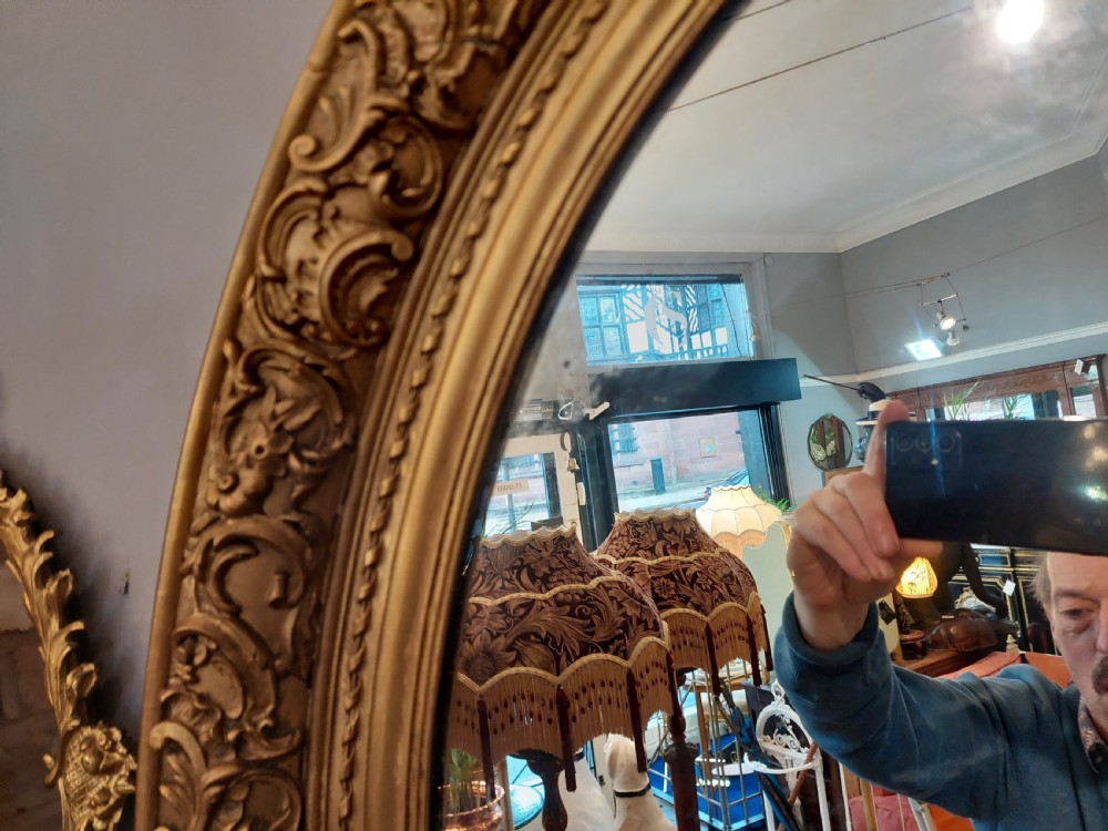 A nineteenth-century oval wall mirror featuring a heavily carved giltwood frame with floral and scrolling moulding details. View VII