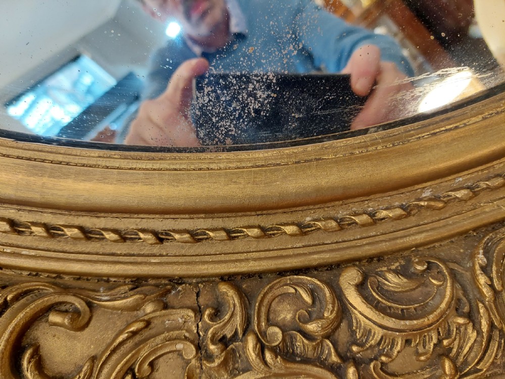 A nineteenth-century oval wall mirror featuring a heavily carved giltwood frame with floral and scrolling moulding details. View VIII