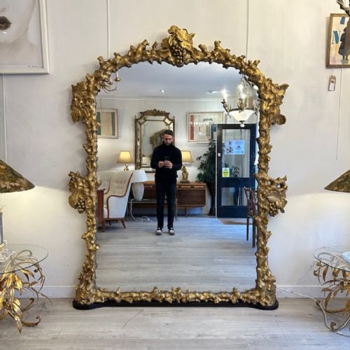 fig 1. An 18th-century Italian giltwood wall mirror featuring a deeply carved frame ornamented with grapevine and leaf motifs surrounding an arched central glass panel.
