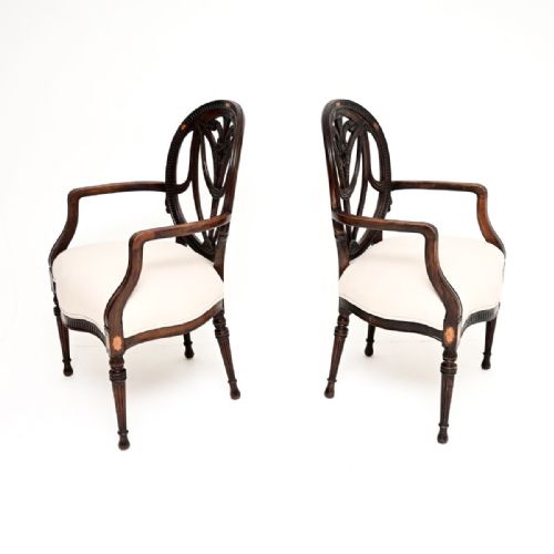 fig 1. A pair of antique Edwardian mahogany carver armchairs featuring oval openwork backs, satinwood floral inlays, shaped armrests, and off-white upholstered seats.