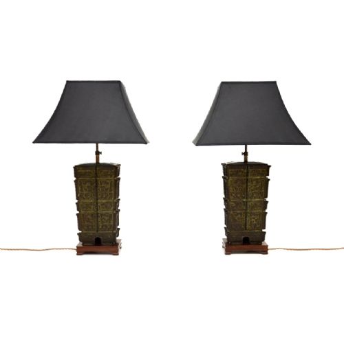 fig 1. A pair of rectangular patinated bronze lamps with relief patternwork mounted on dark wooden bases and topped with black fabric shades.