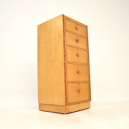 fig 1. A tall Art Deco sycamore chest of drawers featuring five vertical drawers with circular wooden handles and darker wood framed borders.