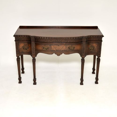 fig 1. An antique dark mahogany server table featuring a serpentine curved front, carved decorative frieze, three drawers with brass handles, and square tapered legs.
