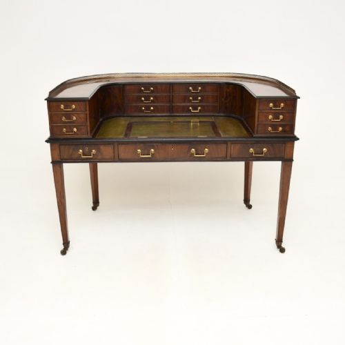 fig 1. An antique inlaid mahogany Carlton House desk featuring a green leather writing surface, multiple small drawers arranged in a horseshoe shape, and a brass gallery rail.