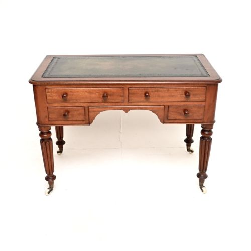fig 1. An antique Victorian mahogany writing desk featuring a green leather top insert, four drawers with turned wooden knobs, and fluted legs on ceramic castors.