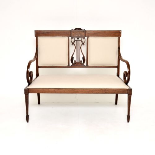 fig 1. An Edwardian inlaid mahogany settee featuring a central lyre splat, sweeping armrests, cream fabric upholstery, and tapered square legs with spade feet.