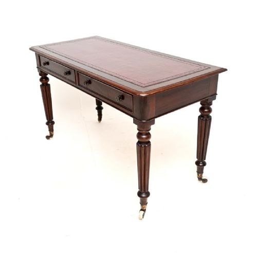 fig 1. An antique Victorian mahogany writing table with a red leather top insert, two front frieze drawers, and reeded turned legs on brass castors.