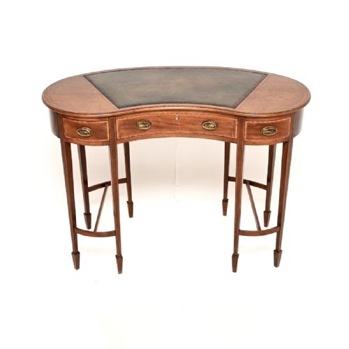 fig 1. An Edwardian mahogany kidney-shaped desk featuring a dark leather writing surface, satinwood inlay, three drawers with brass handles, and slender tapered legs.