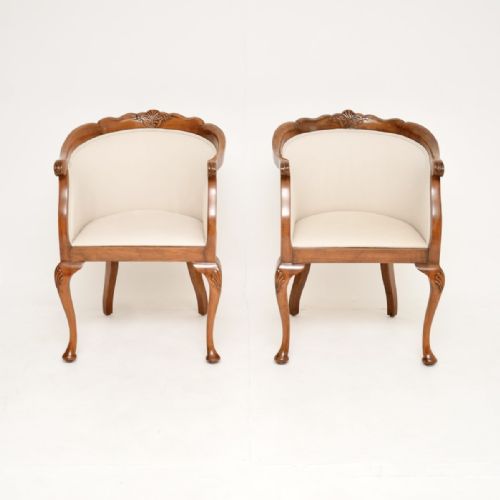 fig 1. A pair of Queen Anne style walnut tub armchairs featuring cream fabric upholstery, carved cresting rails, and cabriole legs with shell motif details.