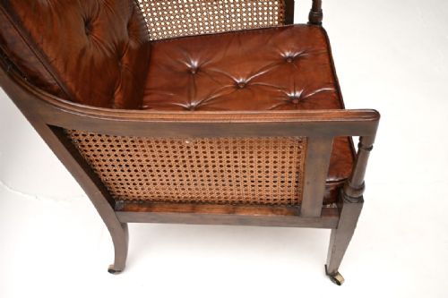 fig 1. An Edwardian mahogany armchair featuring deep-buttoned brown leather cushions, woven cane side panels, and brass castors on tapered legs.