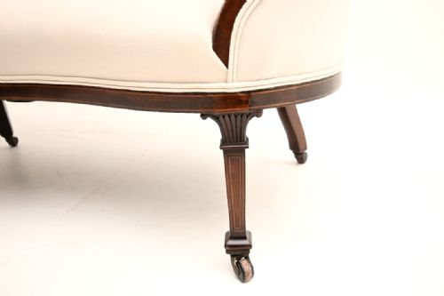 fig 1. An Edwardian inlaid mahogany settee with light cream upholstery, carved back rail detail, and tapered legs fitted with brass castors.