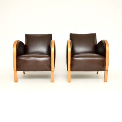 fig 1. A pair of Art Deco armchairs featuring dark brown leather upholstery and sweeping curved satin birch wood armrests on square legs.