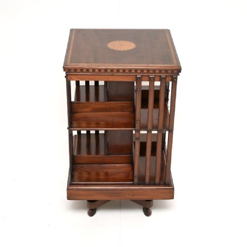 fig 1. An Edwardian inlaid mahogany revolving bookcase featuring a square top with a starburst patera inlay, vertical slatted sides, two tiers of shelving, and a rotating base on brass castors.