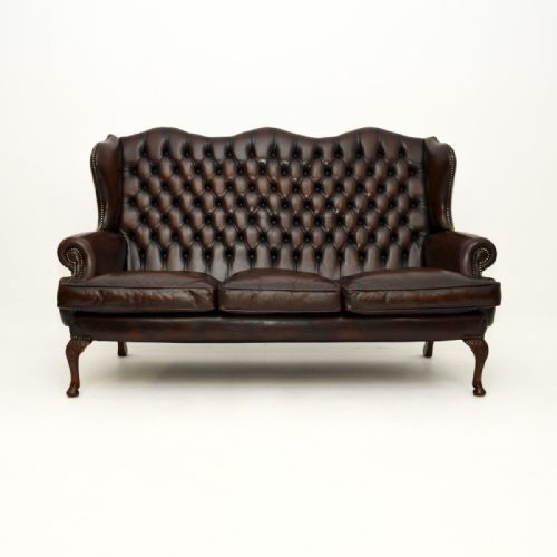 fig 1. A three-seater dark brown leather wingback sofa featuring deep button-tufted upholstery, brass stud detailing, and carved mahogany cabriole legs.