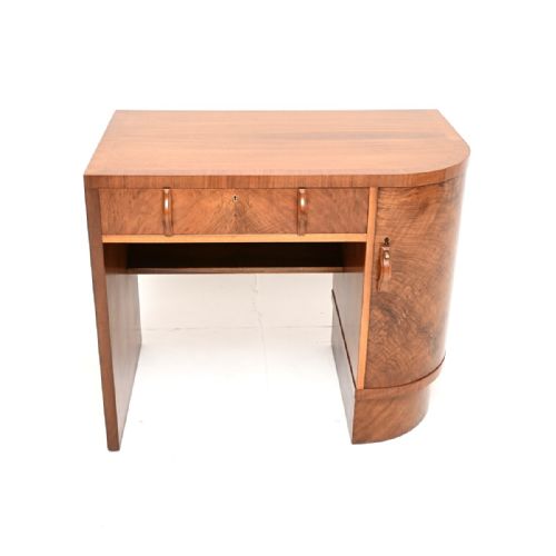 fig 1. An Art Deco writing desk crafted from figured walnut wood, featuring a single top drawer above a kneehole, a curved side cabinet, and carved wooden handles.