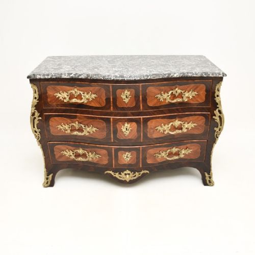 fig 1. A French Louis XV bombee commode featuring dark wood marquetry veneers, ornate gilt-bronze mounts, three drawers, and a contoured grey veined marble top.