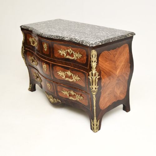 fig 2. A French Louis XV bombee commode featuring dark wood marquetry veneers, ornate gilt-bronze mounts, three drawers, and a contoured grey veined marble top.