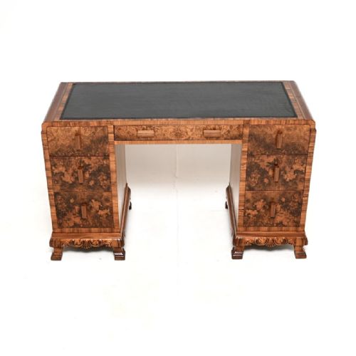 fig 1. An Art Deco twin-pedestal writing desk featuring burr walnut veneer drawers, a black leather top insert, vertical wooden pulls, and carved bracket feet.