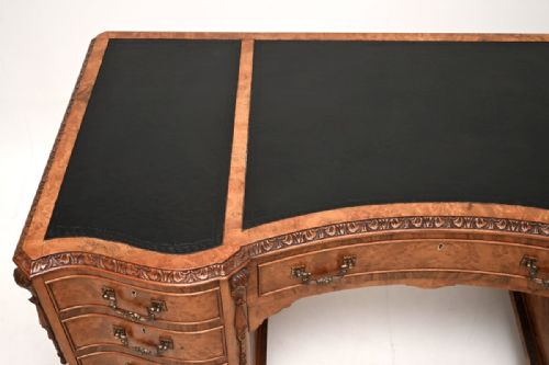 fig 1. A curved burr walnut pedestal desk featuring a three-panel black leather writing surface, nine drawers with brass handles, carved trim, and cabriole legs ending in ball-and-claw feet.