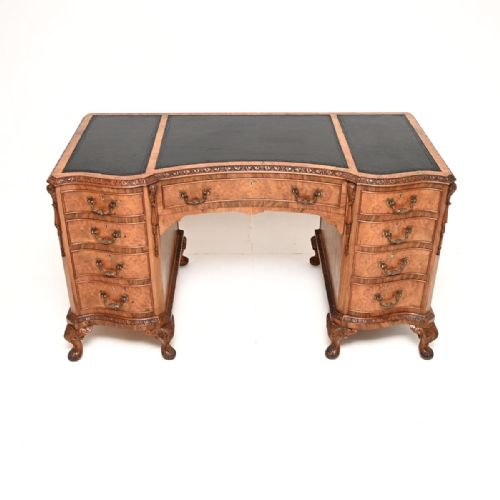 fig 2. A curved burr walnut pedestal desk featuring a three-panel black leather writing surface, nine drawers with brass handles, carved trim, and cabriole legs ending in ball-and-claw feet.