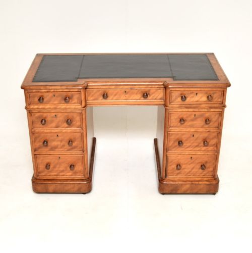 fig 1. A Victorian satinwood pedestal desk featuring a dark leather writing inset, nine drawers with round turned knobs, and a central kneehole.