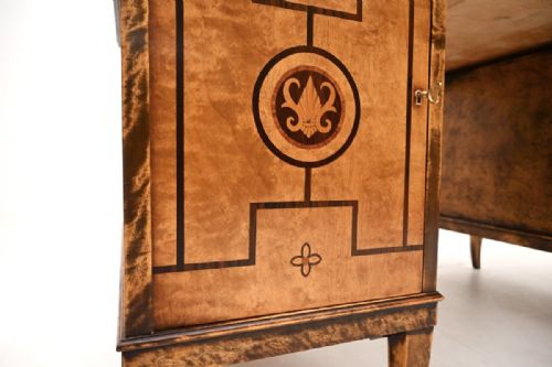 fig 1. An antique Swedish Biedermeier style pedestal desk crafted from figured satin birch with dark wood geometric inlays and tapered legs.
