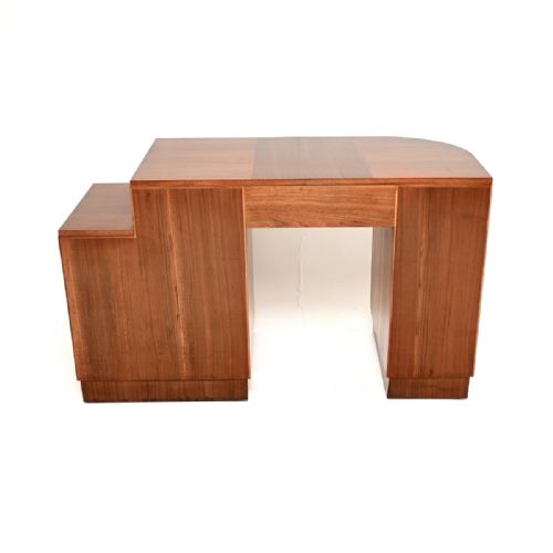 fig 1. An Art Deco figured walnut desk featuring a curved pedestal cabinet, a stack of drawers with rectangular wooden handles, and a central kneehole drawer.