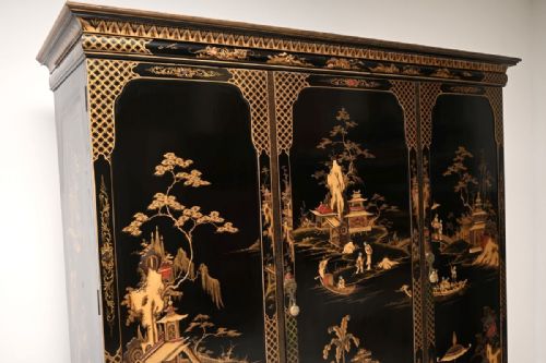 fig 3. A large black lacquered three-door wardrobe decorated with detailed gold chinoiserie landscapes and supported by cabriole feet.
