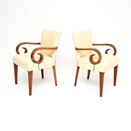 fig 1. A pair of Art Deco armchairs featuring off-white leather upholstery with stud details and curved walnut arms on tapered legs.