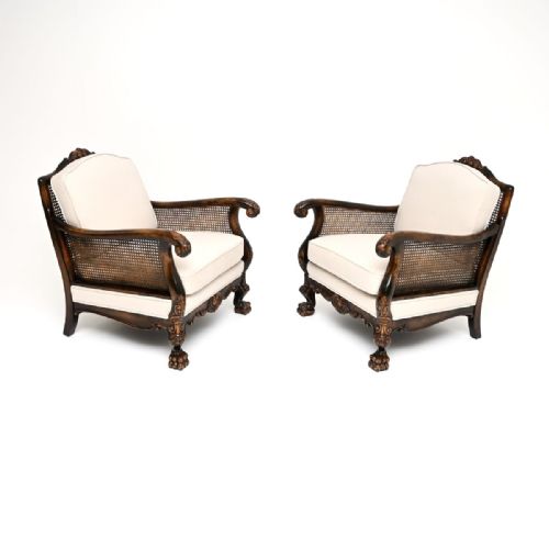 fig 1. A pair of dark carved wood bergere armchairs featuring woven cane sides, paw feet, and light cream upholstered cushions.