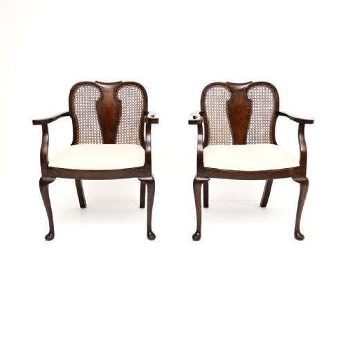 fig 1. A pair of Edwardian dark walnut armchairs featuring woven cane backs with central wood splats, curved armrests, cabriole legs, and off-white upholstered seats.