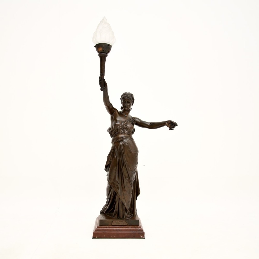 A dark patinated French bronze classical female figure holding aloft a torch light fixture with a flame glass shade, set on a red marble base.