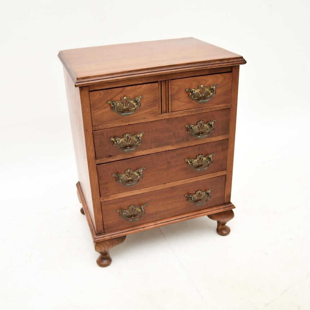 An antique walnut chest of drawers featuring a two short over three long drawer arrangement, decorative brass handles, and shaped feet.