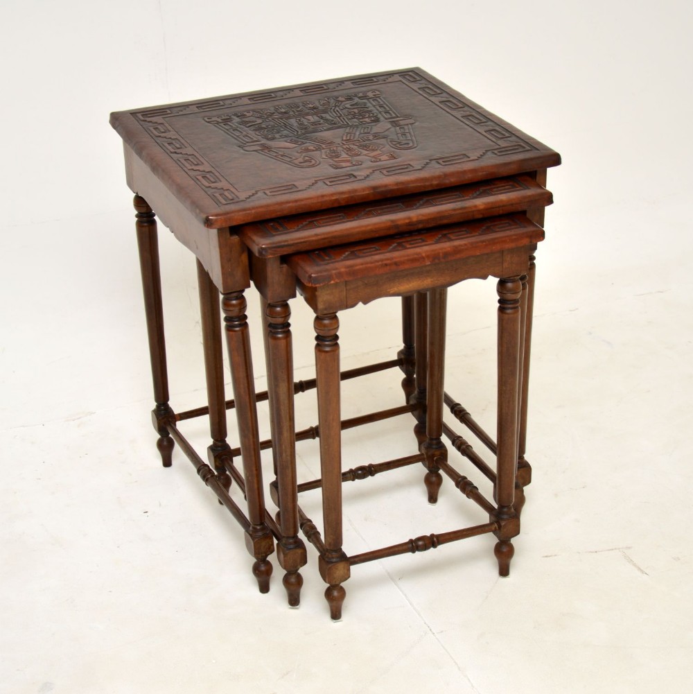 A set of three dark wood nesting side tables featuring turned legs, horizontal stretchers, and embossed leather tops decorated with geometric motifs.