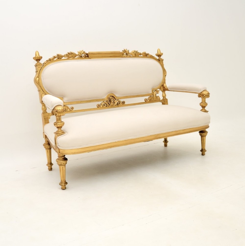 A Swedish Empire giltwood settee featuring a carved leaf crest, finials, fluted legs, and neutral cream upholstery.