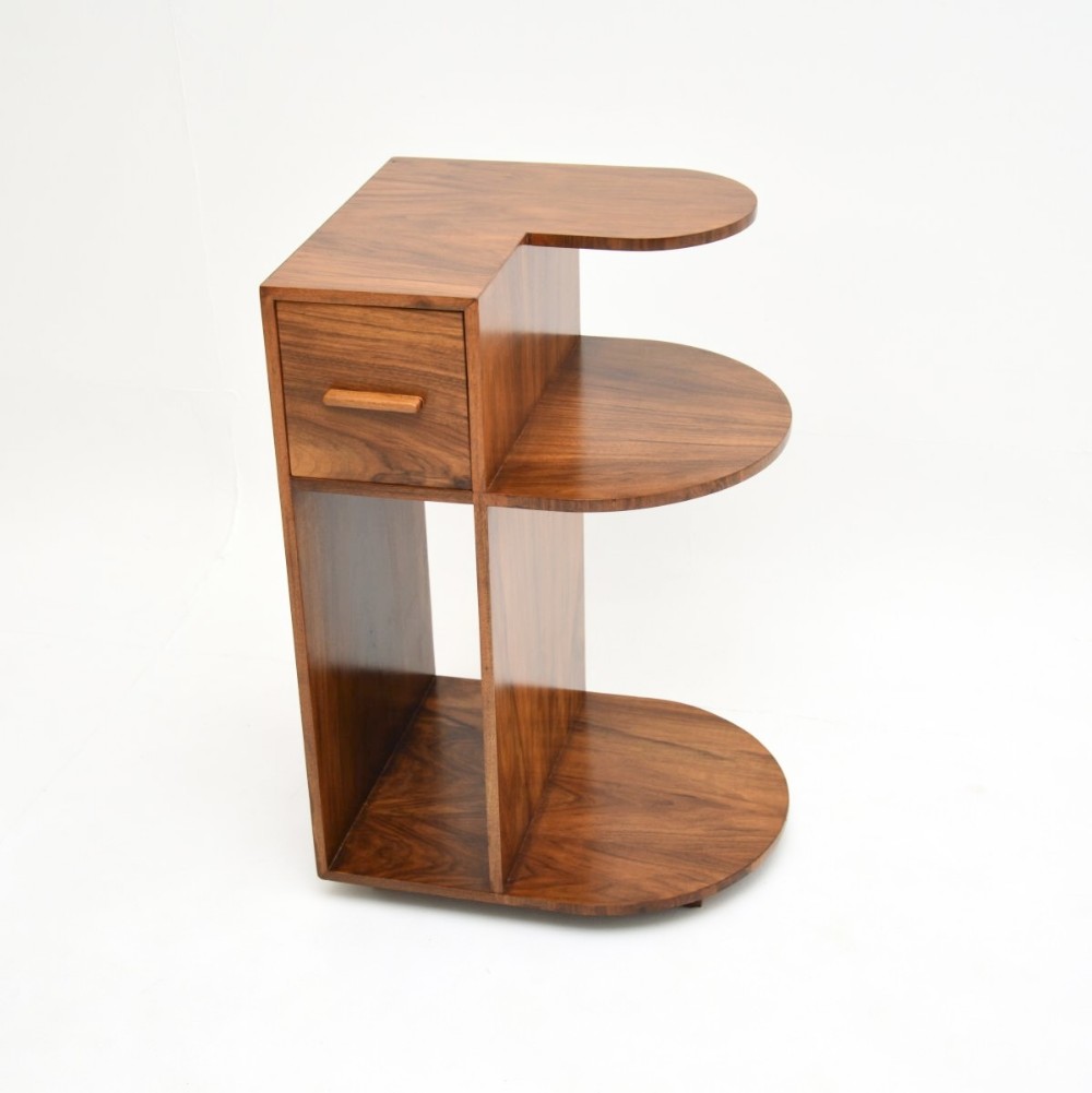 An Art Deco figured walnut side table featuring an asymmetrical design with a single drawer and tiered curved shelves.