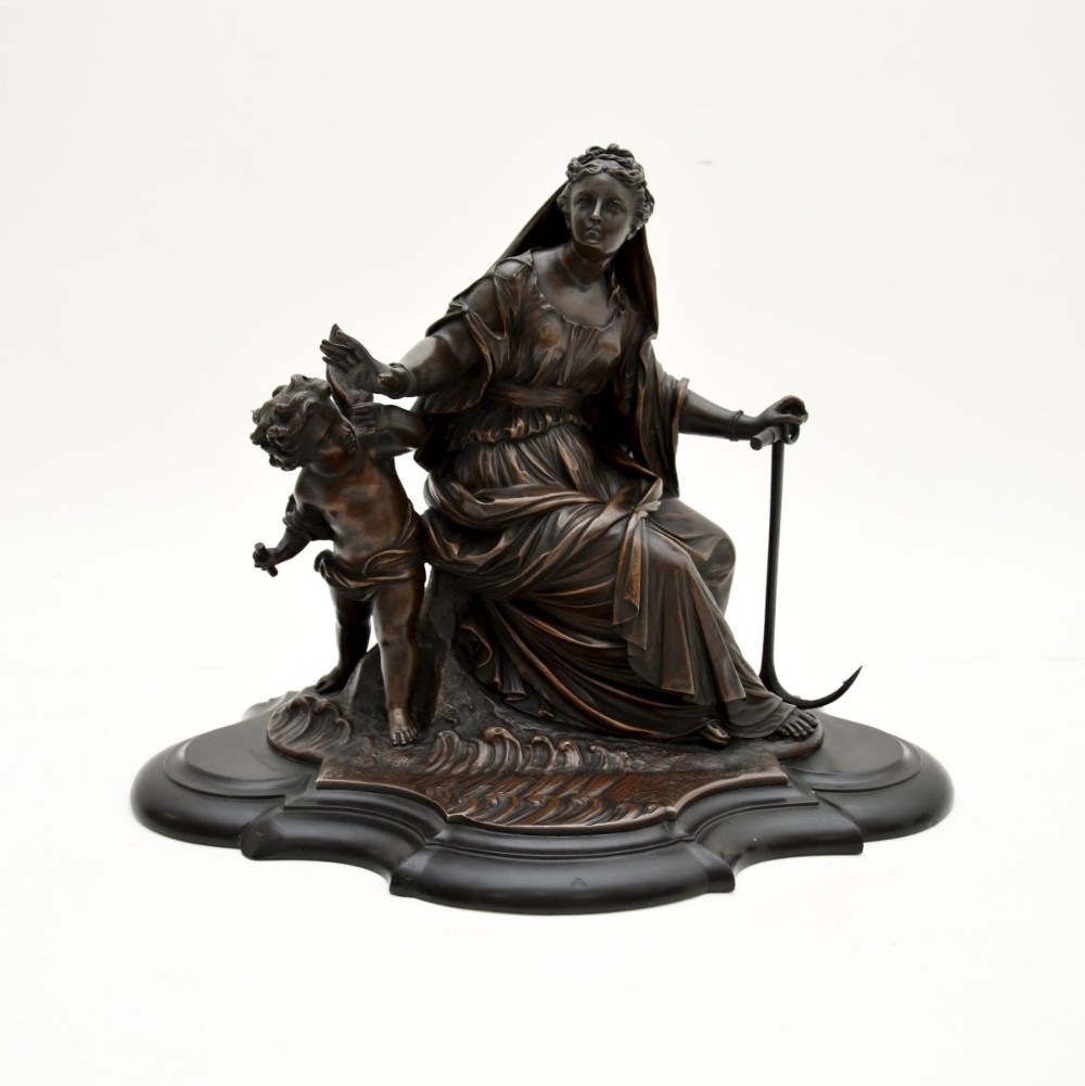A dark patinated bronze classical sculpture depicting a draped female figure seated alongside a child on a shaped wooden base.