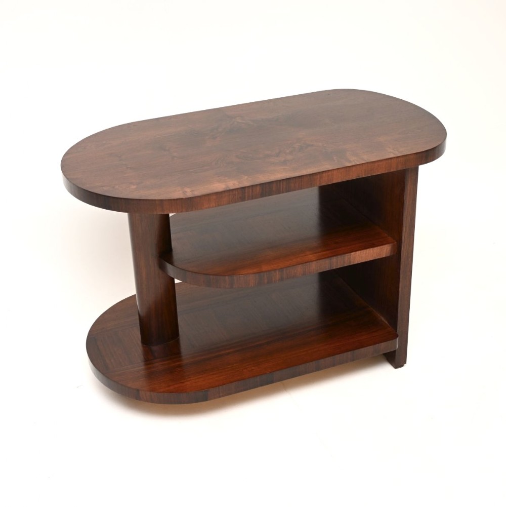 An Art Deco rosewood side table featuring an oval top, two lower open shelves, a support column, and a flat side panel in a polished dark wood grain.