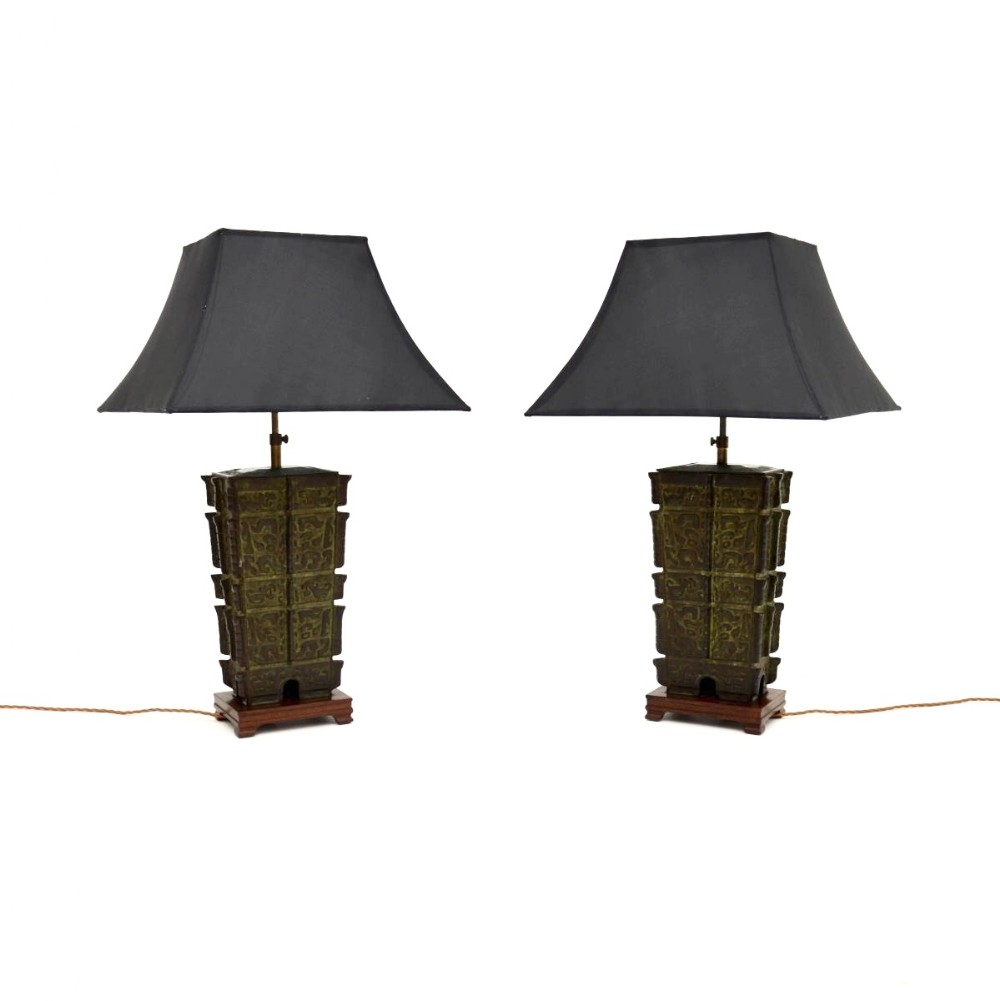 A pair of rectangular patinated bronze lamps with relief patternwork mounted on dark wooden bases and topped with black fabric shades.